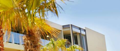 A modern building with balconies and a palm tree in the foreground.