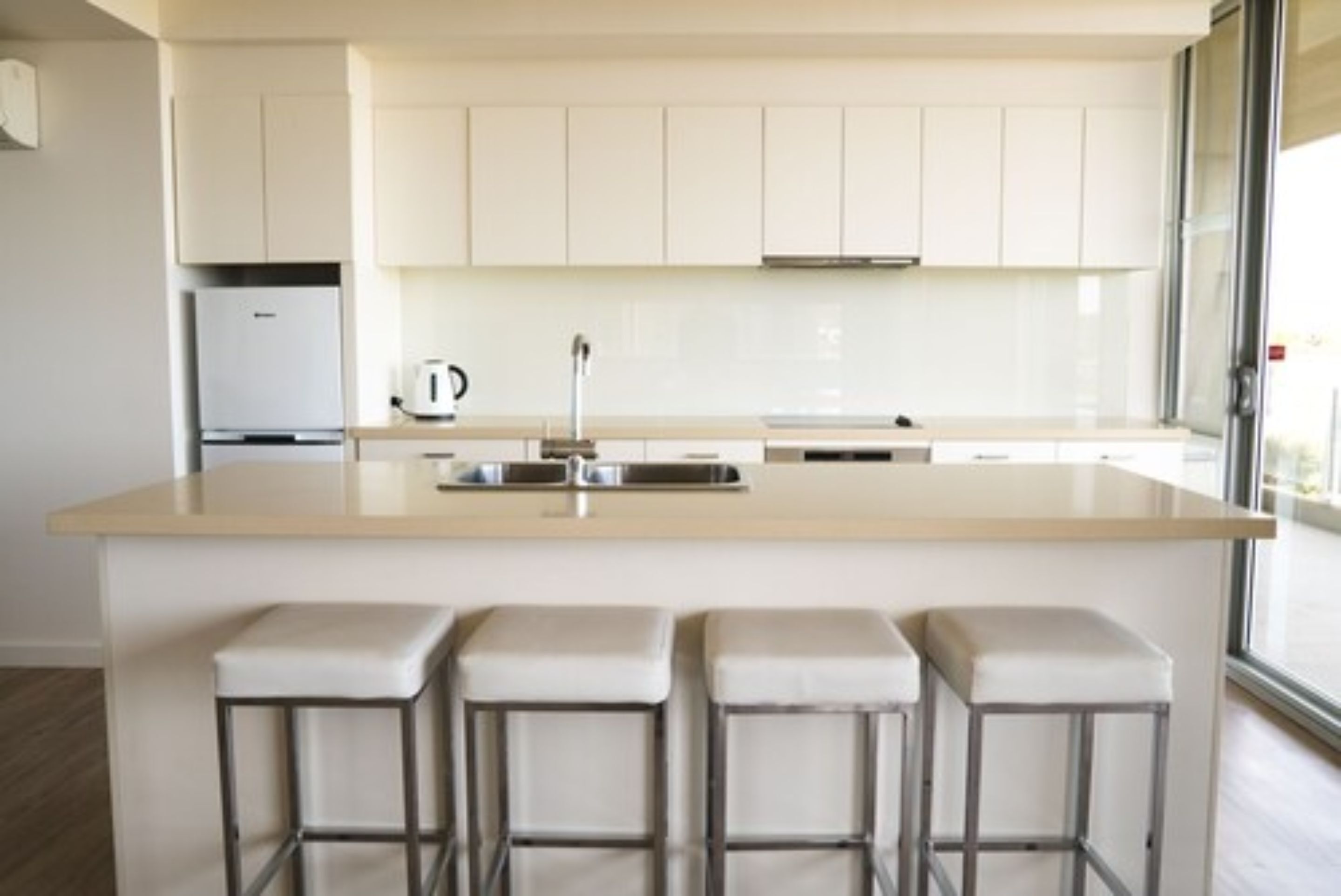 Una cocina moderna con armarios blancos, una isla central con taburetes y un amplio ventanal que proporciona luz natural.