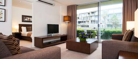 A modern hotel room with a sofa, a coffee table with flowers, a TV, and a balcony with a view of the city.