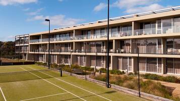 A multi-story hotel with balconies, a tennis court, and a landscaped garden area.