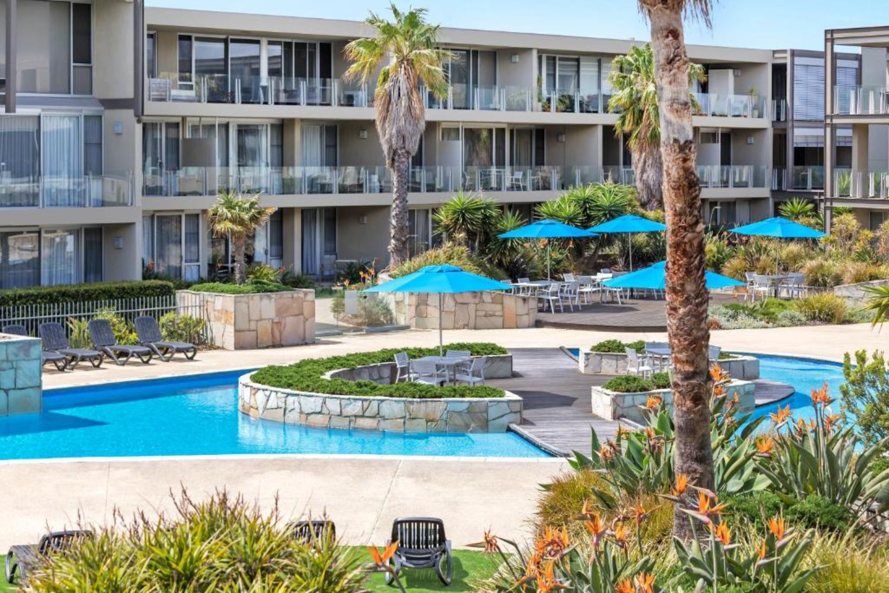 Un hotel con piscina, mobiliario exterior y un jardín ajardinado.