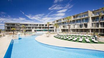 A hotel with a swimming pool, sun loungers, and palm trees.