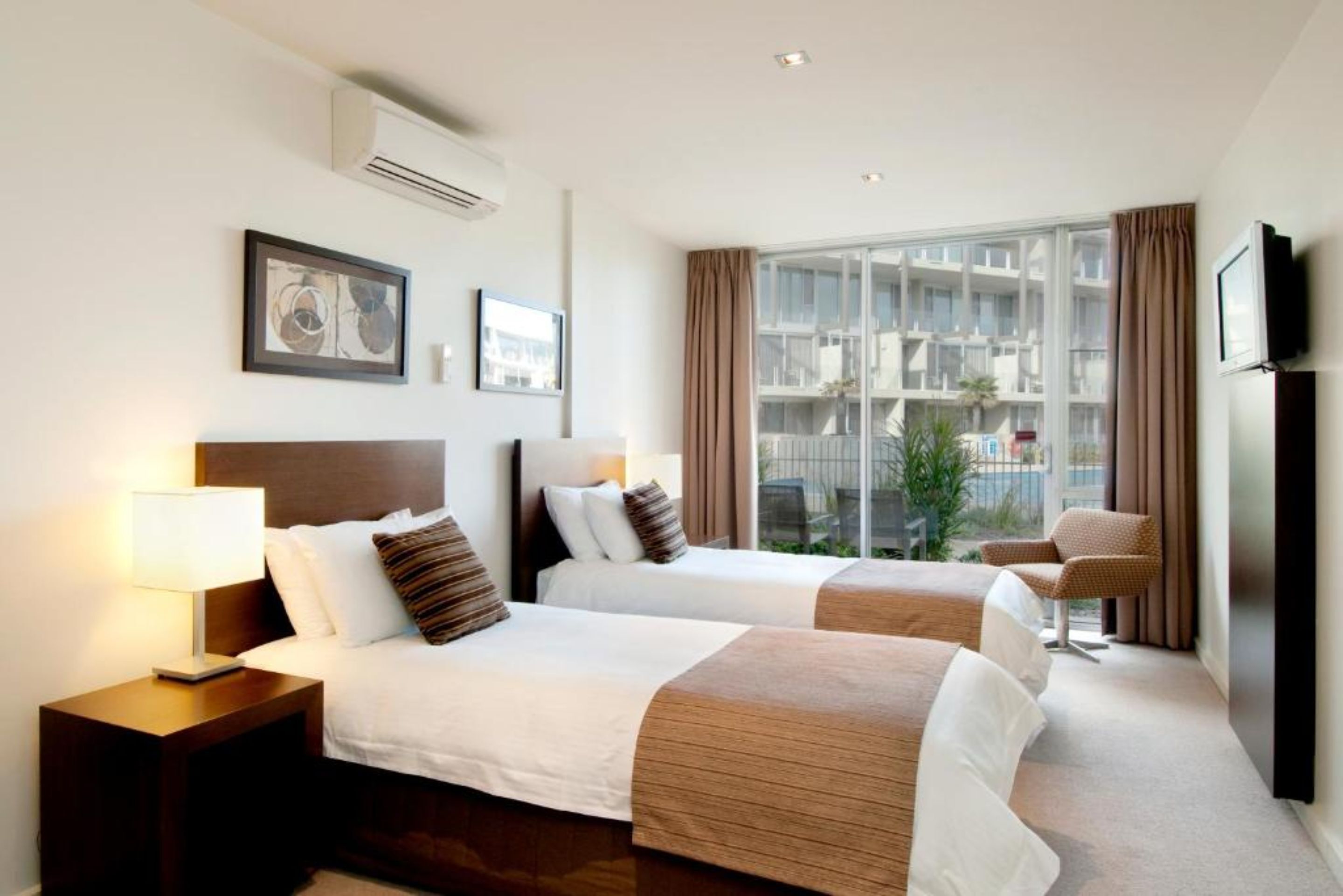 A hotel room with two beds, a TV, a window with curtains, and artwork on the wall.