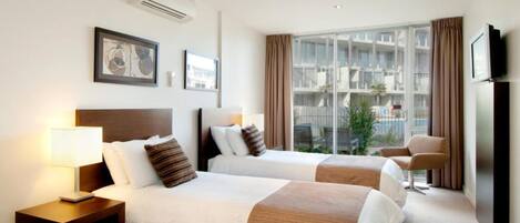 A hotel room with two beds, a TV, a window with curtains, and artwork on the wall.