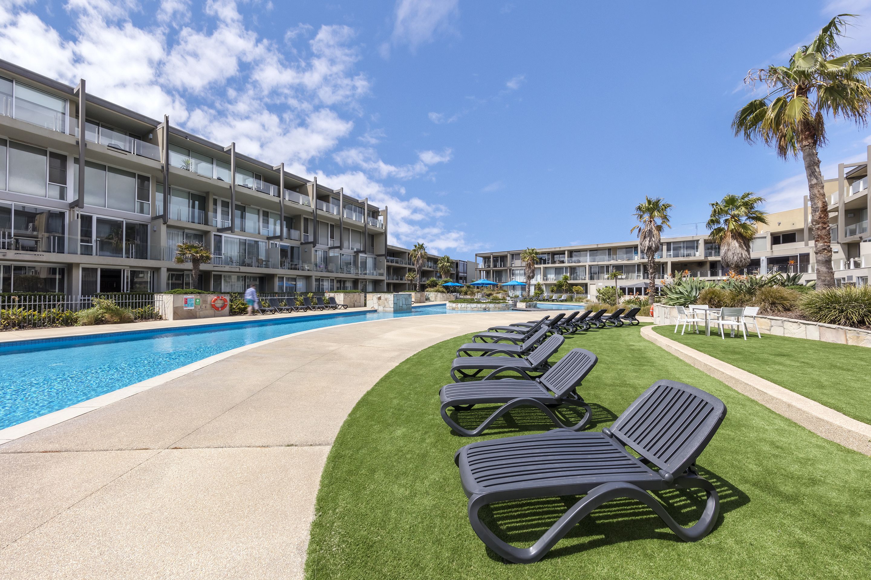 A hotel with a swimming pool, sun loungers, and palm trees.