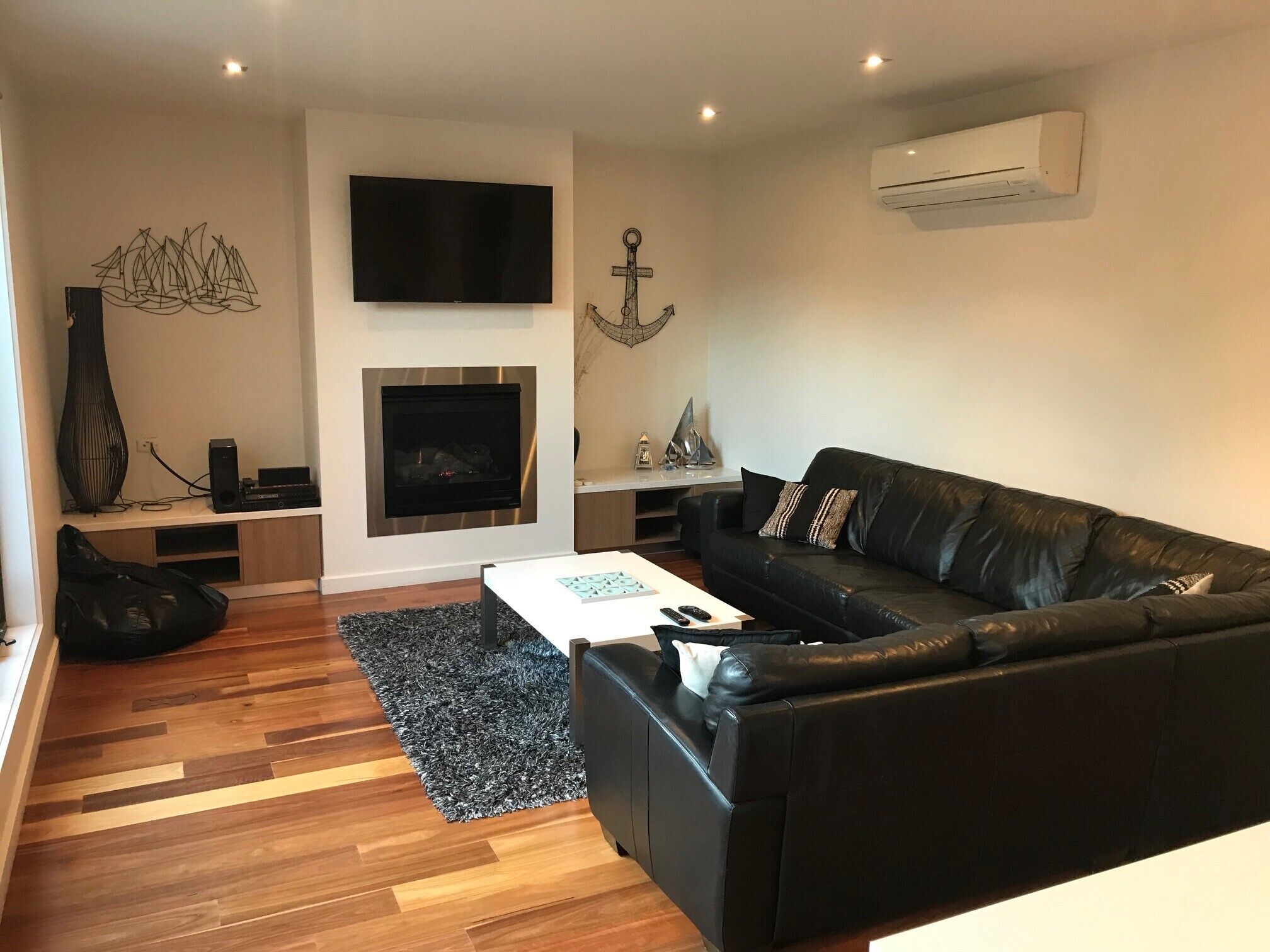 A modern living room with a black leather sofa, a flat-screen TV, a fireplace, and a wooden floor.