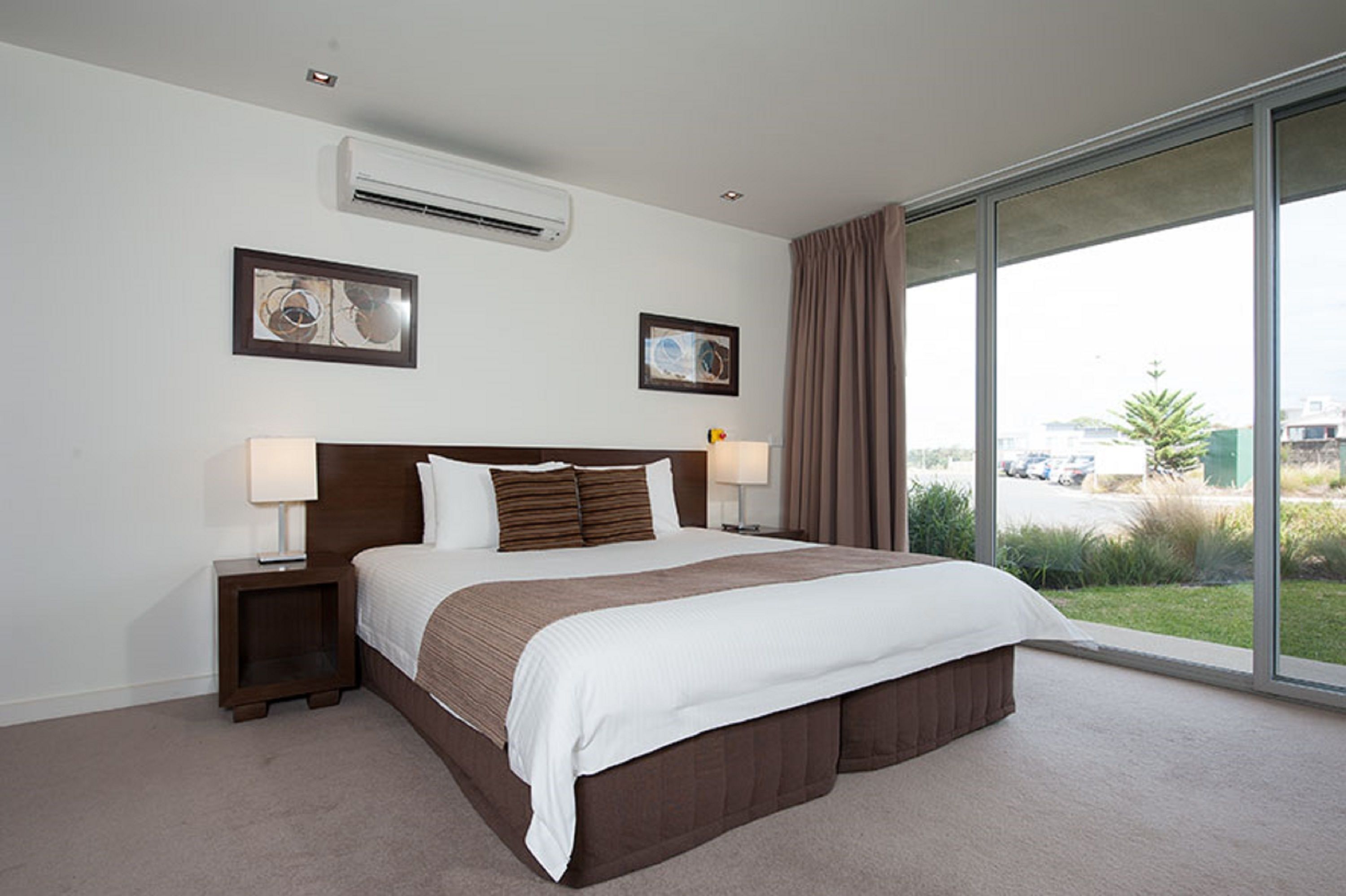 Una habitación de hotel con una cama grande, dos mesitas de noche, un equipo de aire acondicionado y vistas al exterior.