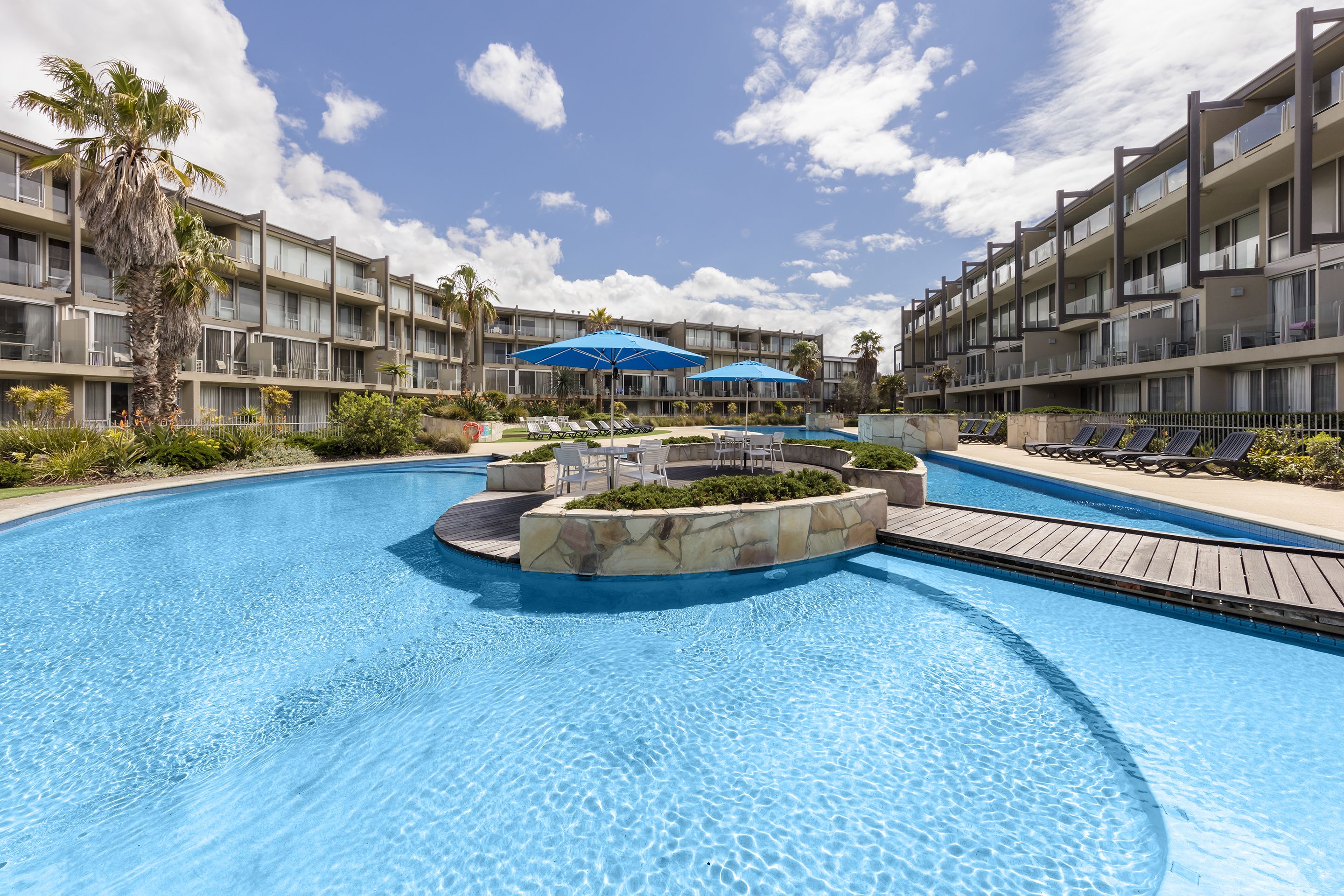 A hotel with a swimming pool, sun loungers, and a palm tree.
