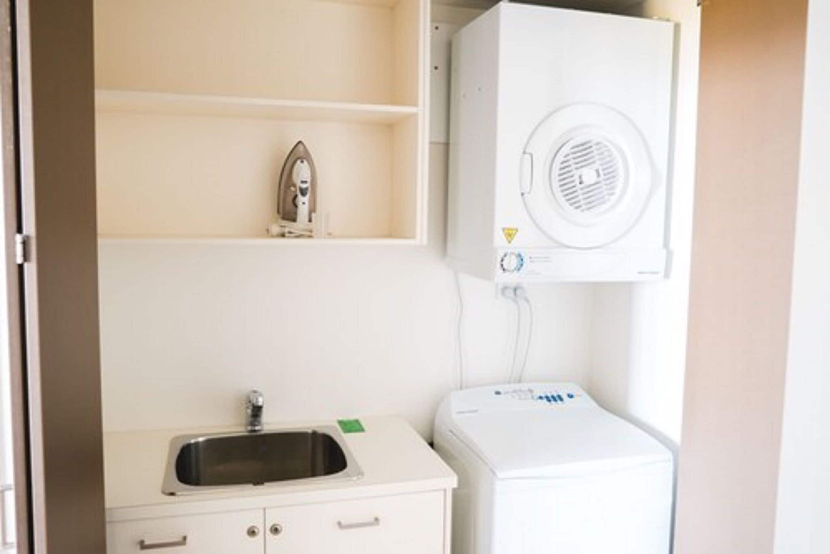 Een compacte kitchenette met een spoelbak, een strijkijzer en een kleine wasmachine.