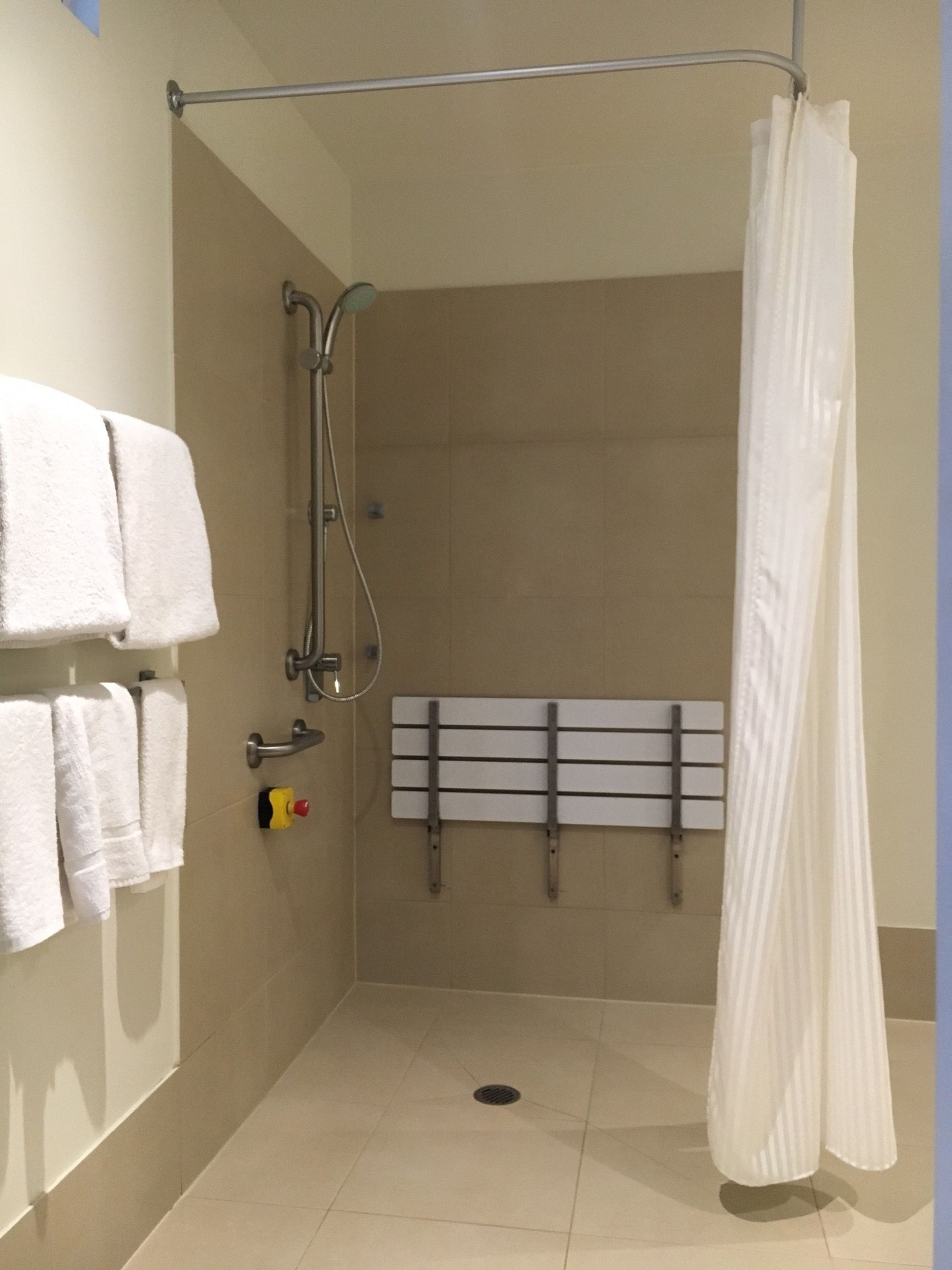 Zona de ducha con cortina blanca, un perchero con toallas blancas y un toallero de pared.