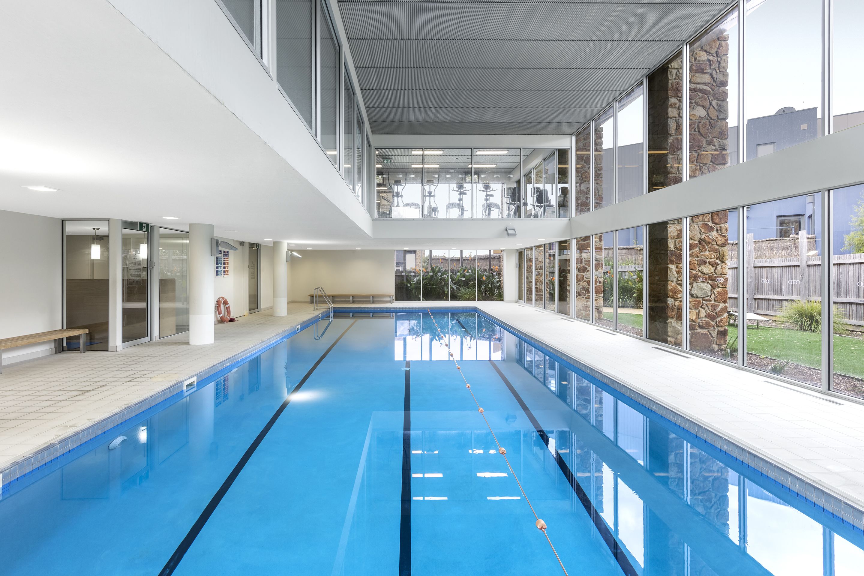 Una piscina interior con paredes de vidrio transparente, un banco y vistas al exterior.