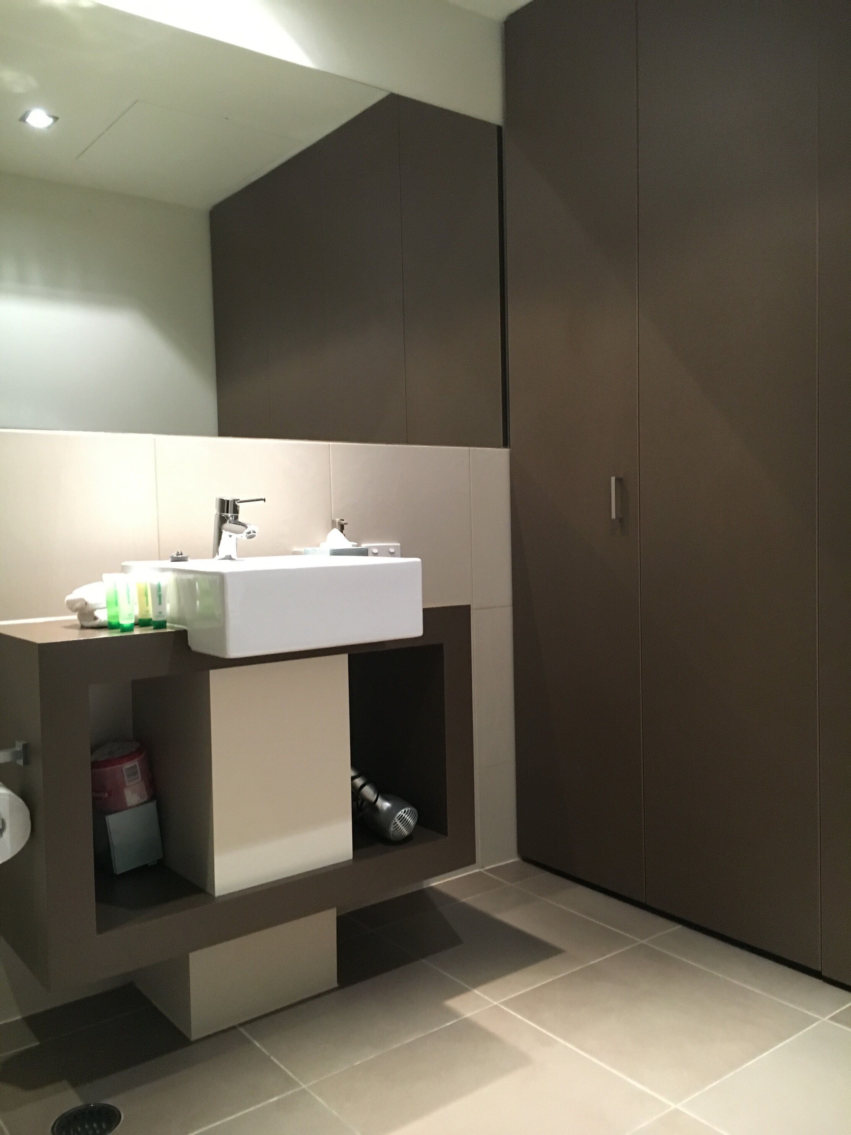 Un baño moderno con un espejo grande, un lavamanos blanco y un mueble empotrado.