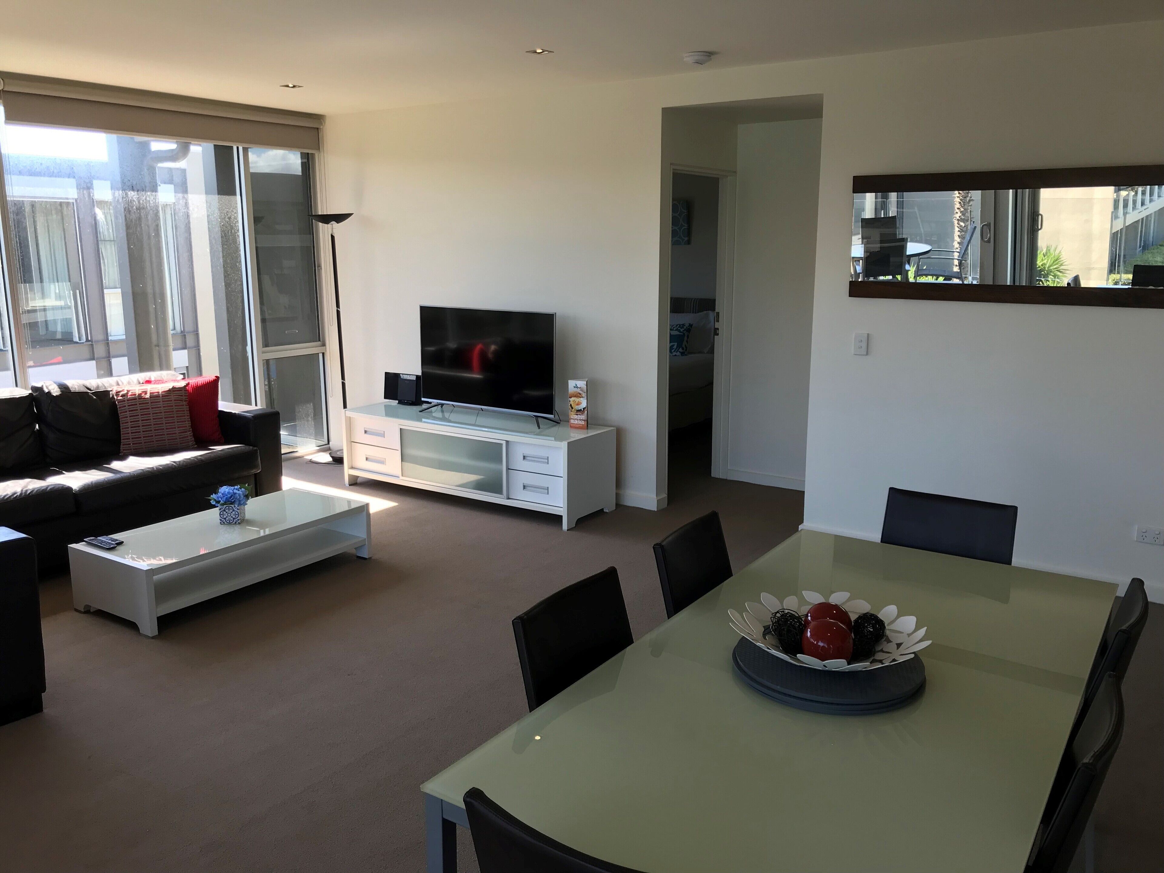 A modern living room with a sofa, TV, coffee table, and dining area.