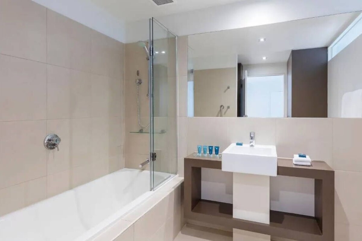 A modern bathroom with a glass-enclosed shower, a white bathtub, and a vanity with a sink and mirror.