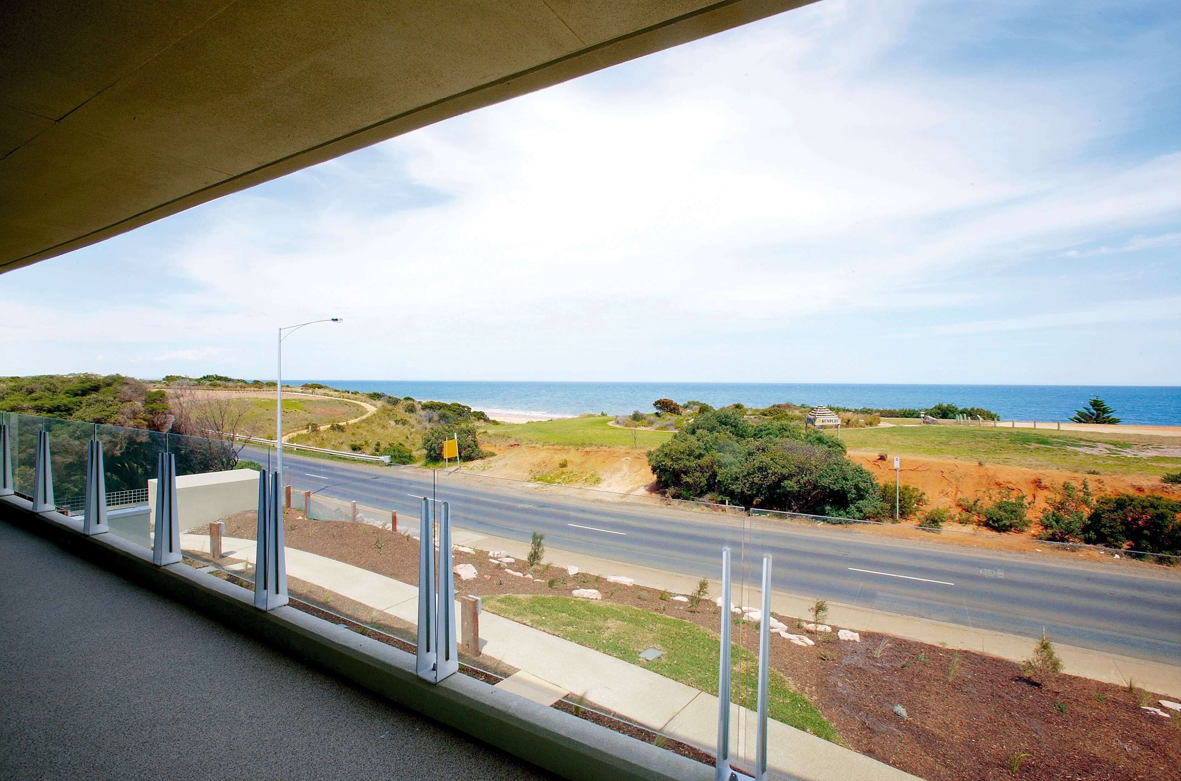 A coastal road with a clear view of the ocean and a grassy area with a sign.
