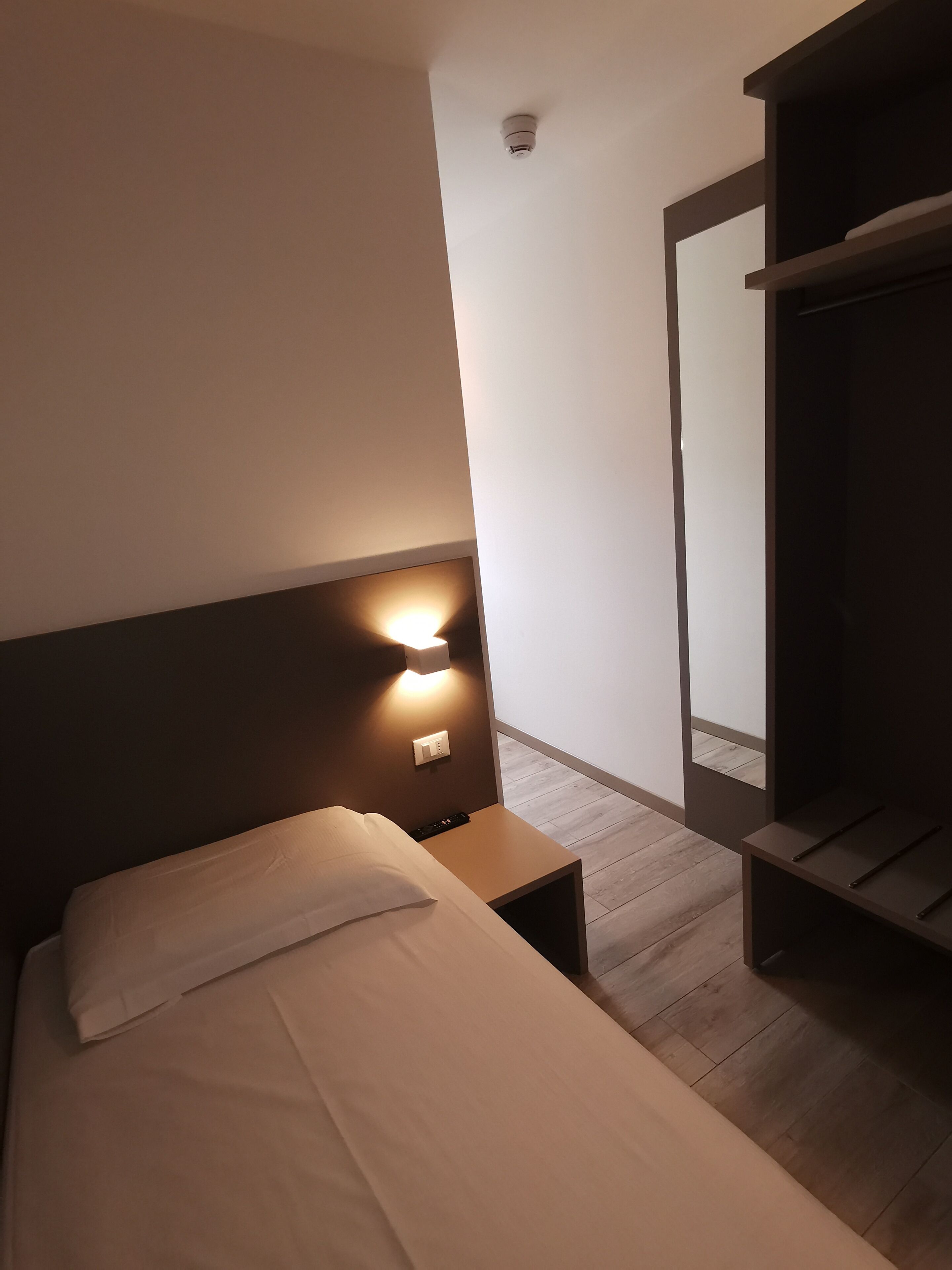 A hotel room with a bed, bedside table, wall-mounted light, and a window with a view.