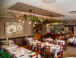 Restaurante com mesas preparadas para refeições, área de bar e uma grande obra de arte floral na parede.