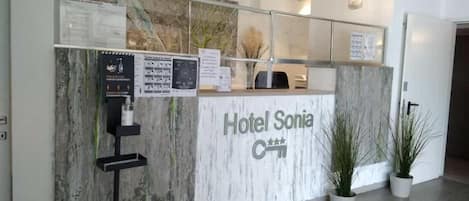 Mostrador de recepción en el Hotel Sonia, con diseño de mármol, pantalla digital y plantas en macetas.