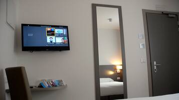Una habitación de hotel con una cama, una silla, un televisor montado en la pared y un estante con libros.