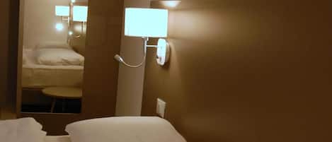 A hotel room with a bed, a bedside table, and a wall-mounted light fixture.
