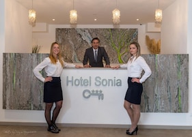 Bancada de recepção do Hotel Sonia com design moderno, uma grande pintura abstrata na parede e um candelabro acima.