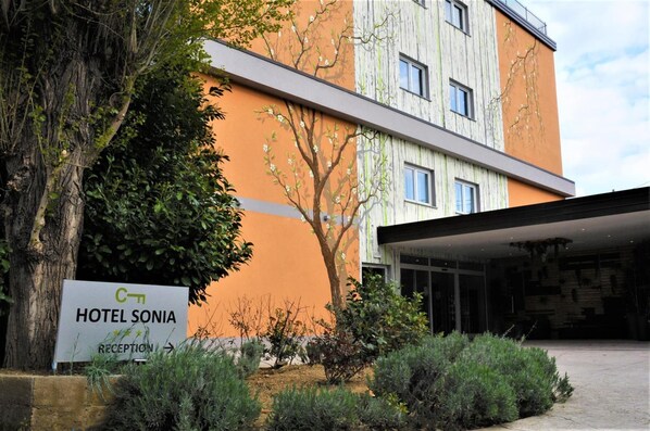 En moderne hotelbygning med et reception område, et skilt med navnet "HOTEL SONIA", og et træ i forgrunden.