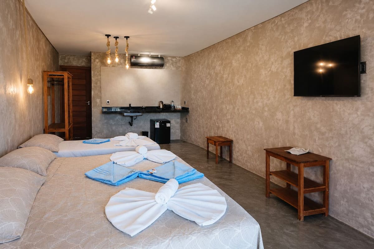 Habitación de hotel con cama, toallas, una mesita, televisor y kitchenette.