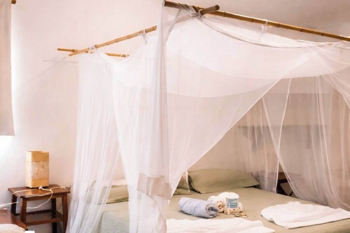 Una habitación con una cama bajo un dosel, una mesita de noche y una lámpara.