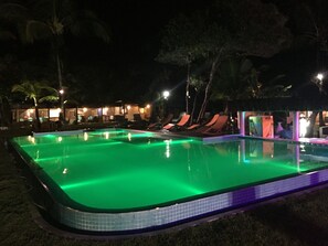 A nighttime swimming pool with green lighting, surrounded by lounge chairs and palm trees. - Arraial Praia Hotel Pousada (Porto Seguro)