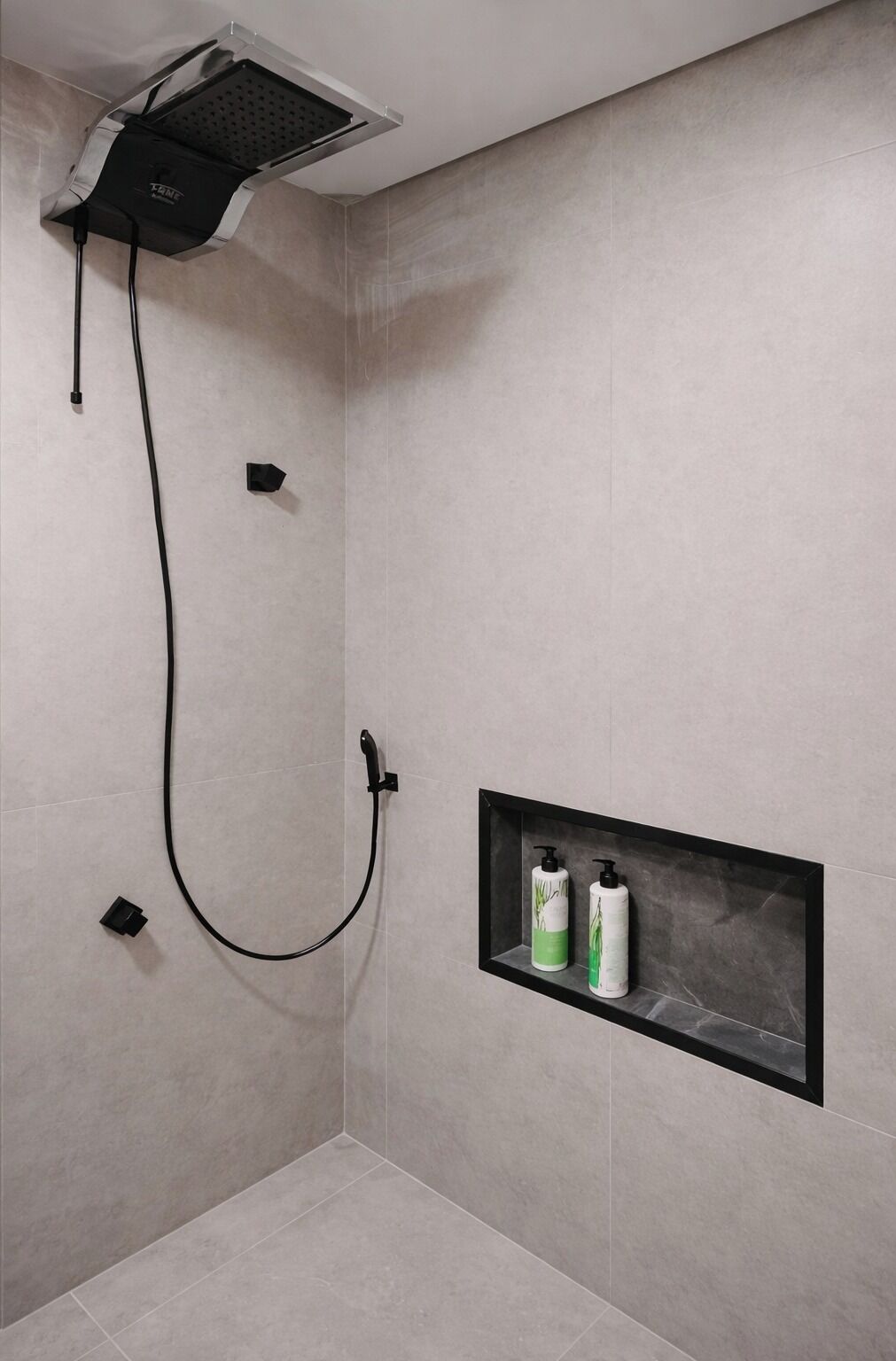 A shower with a handheld showerhead, a wall-mounted control panel, and a shelf with toiletries.