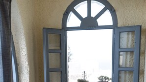 A small, enclosed patio area with a wooden table and two chairs, a window with shutters, and potted plants on the windowsill. - Aspa Villas (Santorini)