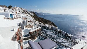 A seaside terrace with white buildings, a blue door, and a view of the ocean. - Aspa Villas (Santorini)