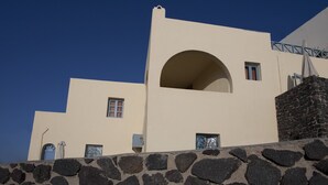 A building with a stone wall, a large arched window, and a blue door. - Aspa Villas (Santorini)