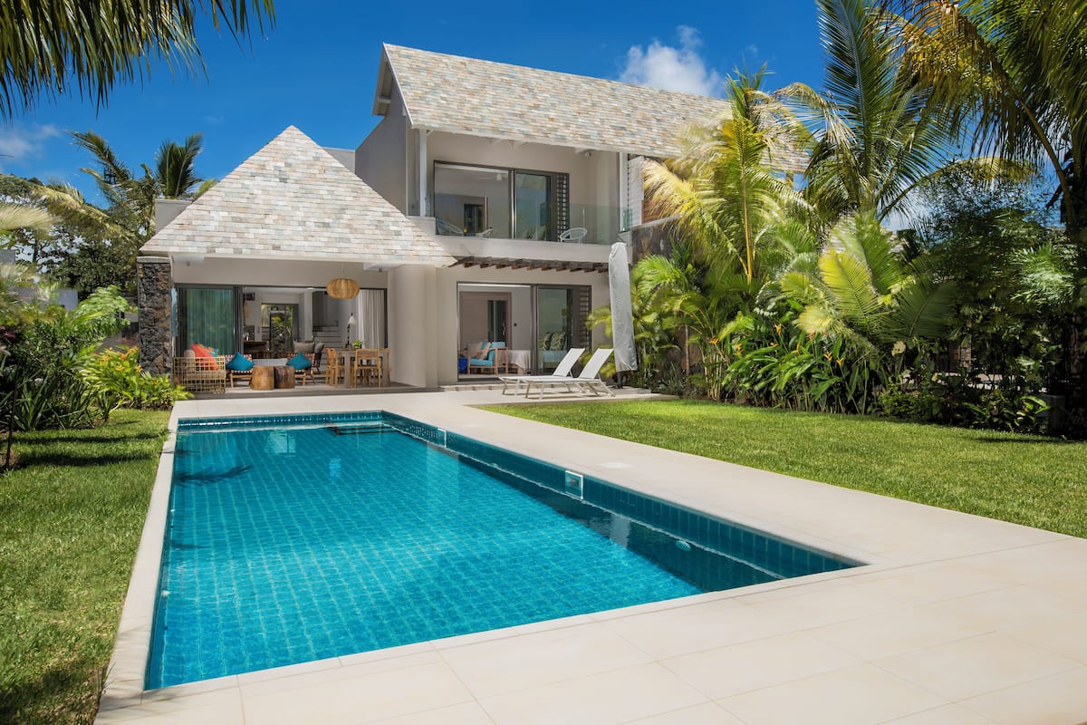 A two-story house with a swimming pool, outdoor furniture, and lush greenery.