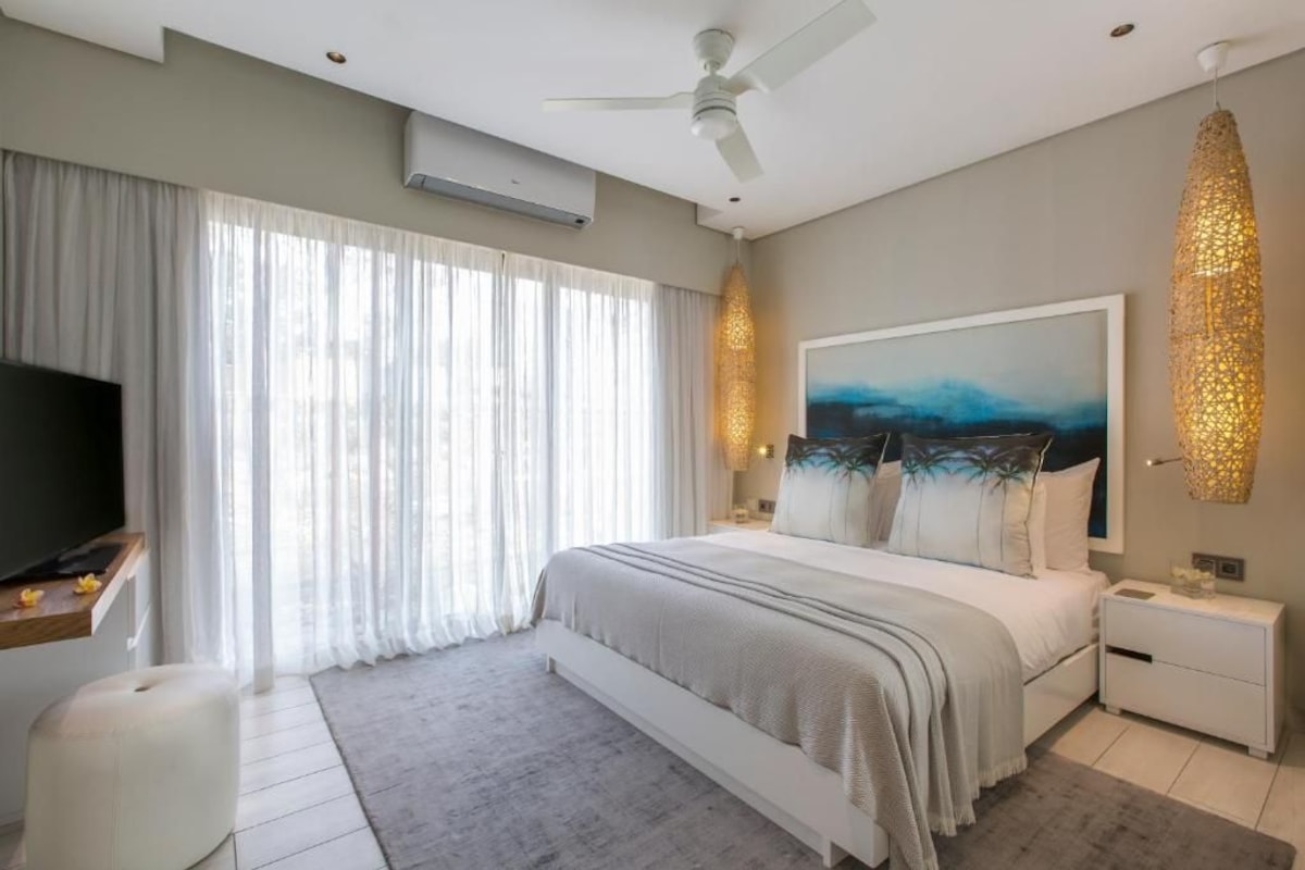 Un dormitorio moderno con una cama grande, un ventilador de techo, un televisor y un cuadro en la pared.