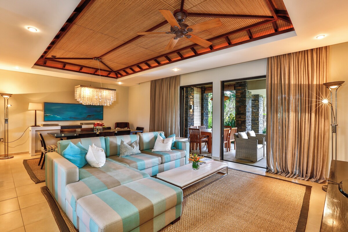 A modern living room with a sectional sofa, a flat-screen TV, and a dining area with a view of the outdoors.