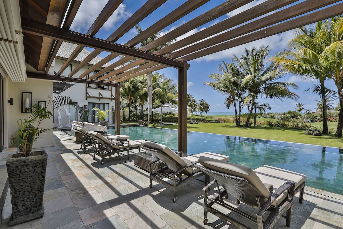 A poolside area with lounge chairs, a pergola, and a view of the ocean.