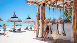 A beach with wooden swings, thatched umbrellas, and lounge chairs. - The Bay Club at Anahita (Grand River South East)