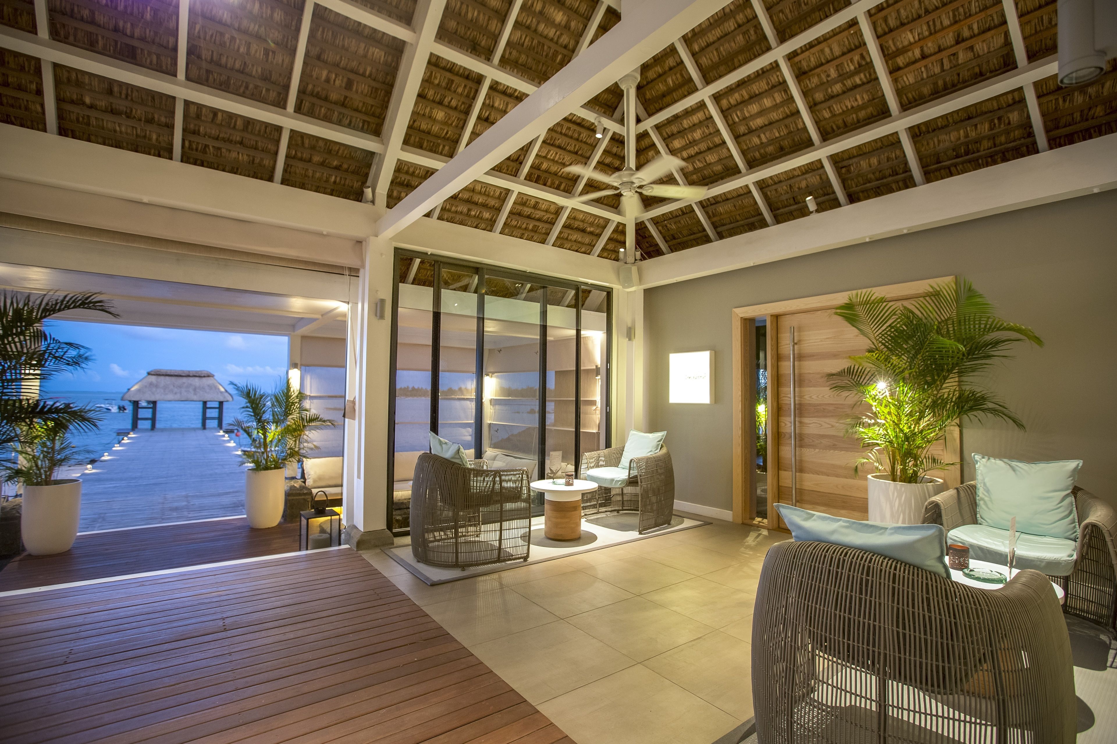 A spacious indoor area with a wooden deck leading to a glass door, wicker furniture, and a ceiling fan.