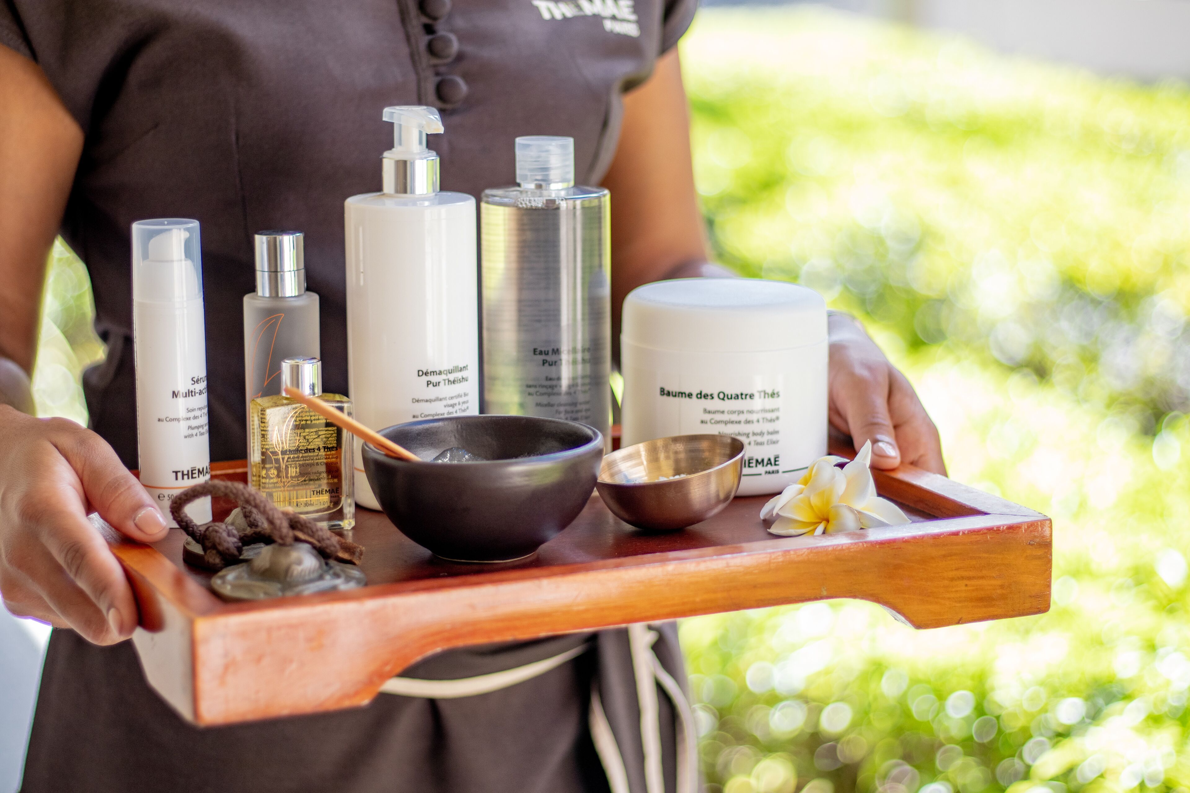A tray with various skincare products, including bottles and a bowl, held by a person.