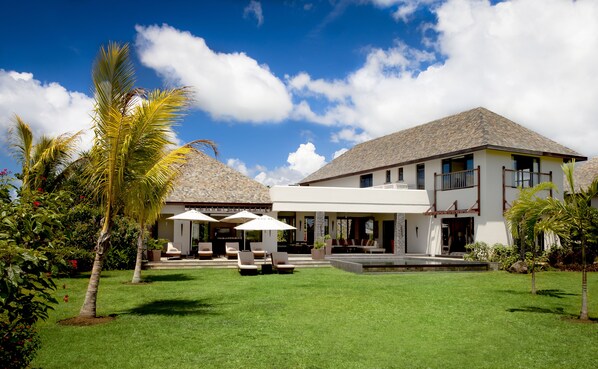 A modern house with a spacious patio, outdoor seating, and a well-maintained lawn. - The Bay Club at Anahita (Grand River South East)