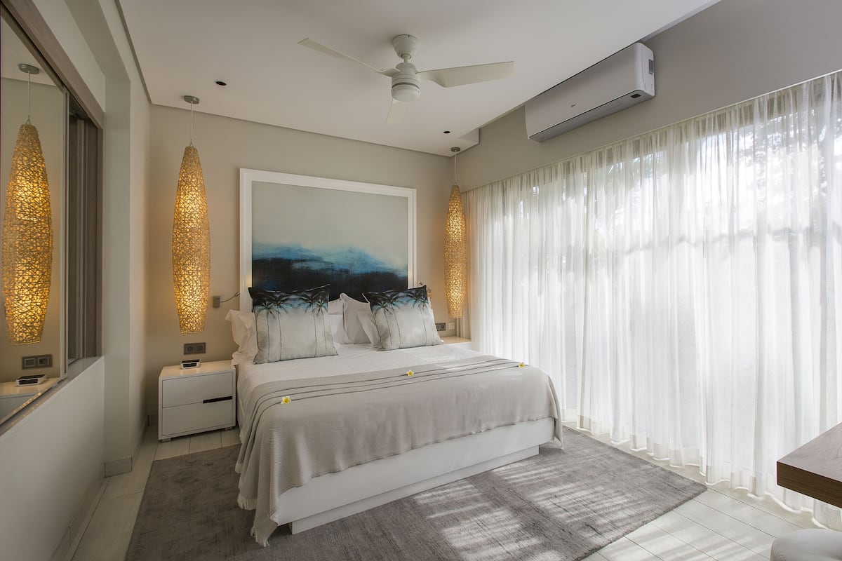 A modern bedroom with a large bed, bedside tables, a ceiling fan, and a large window with sheer curtains.