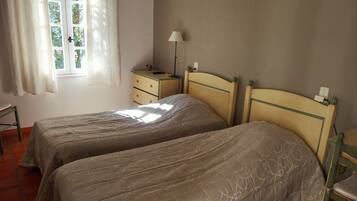 A bedroom with two beds, a nightstand, a lamp, and a window with curtains.