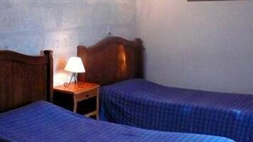 Una habitación con dos camas, cada una con cubrecama azul, una mesita de noche con lámpara y un cuadro en la pared.