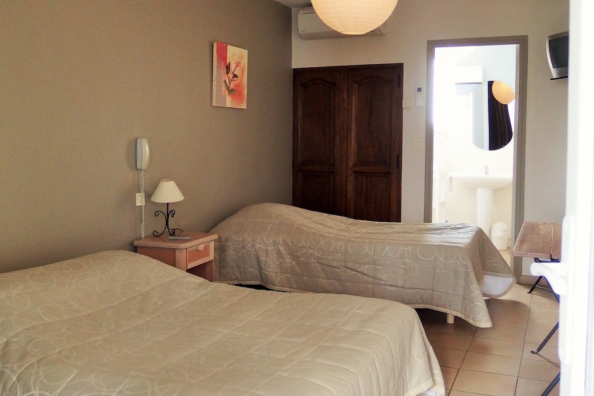 A hotel room with two beds, a bedside table with a lamp, a wall-mounted phone, and a painting.