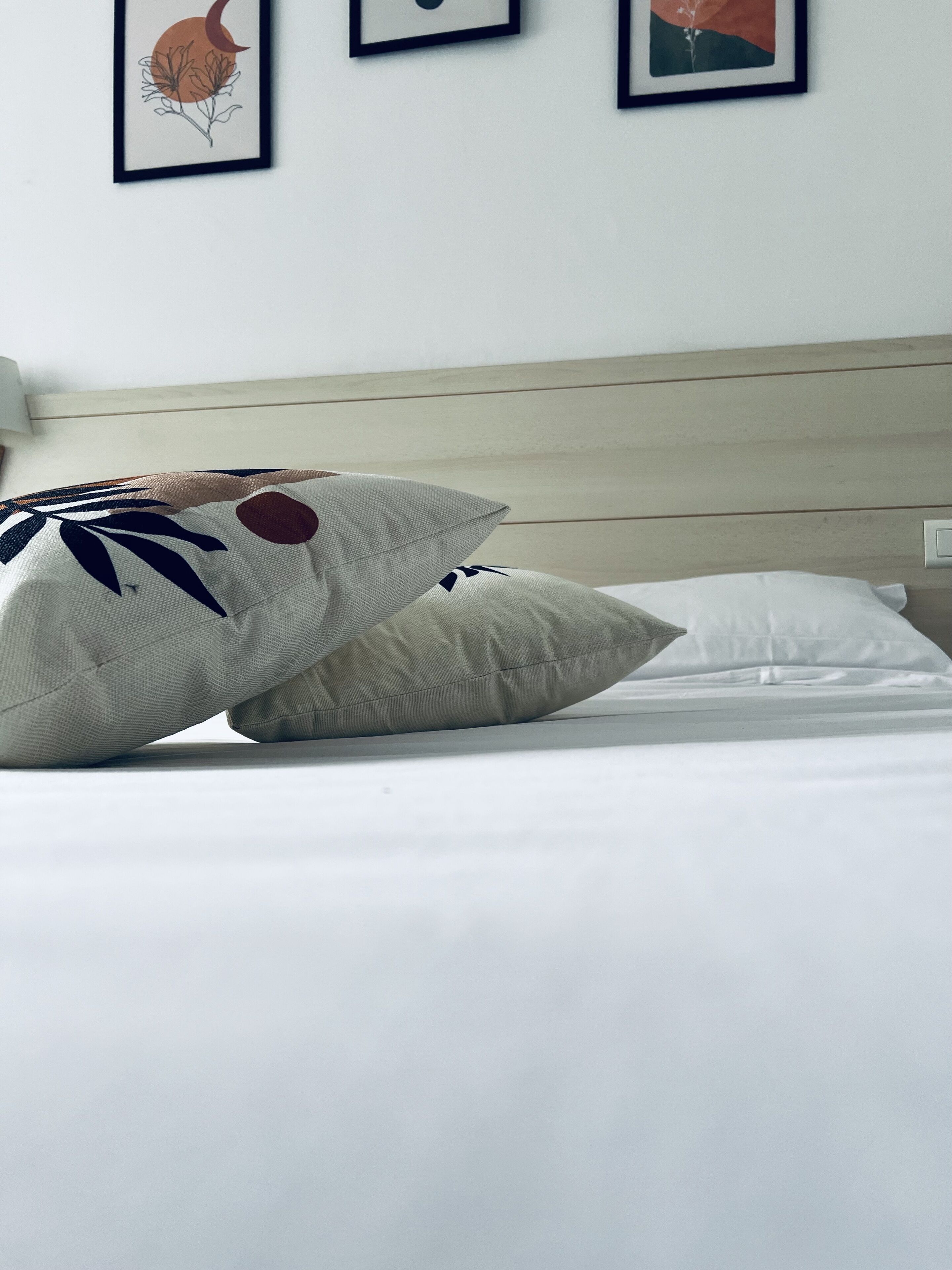 Ein ordentlich gemachtes Bett mit weißen Laken und zwei Zierkissen, eines mit einem Blattmuster und das andere schlicht.