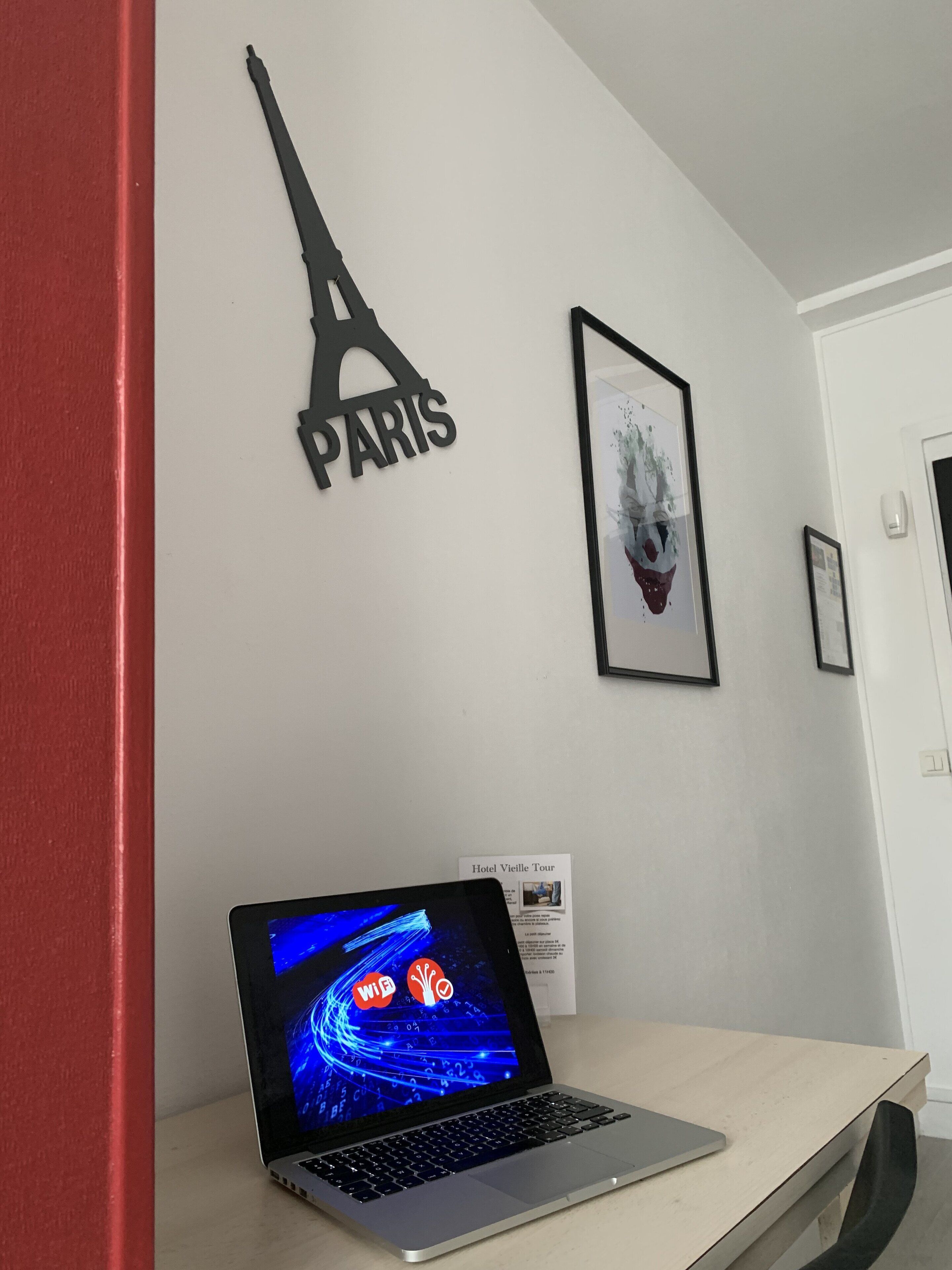 A laptop on a desk with a framed picture of the Eiffel Tower and a framed artwork on the wall.