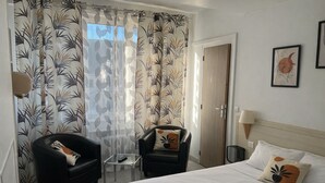A hotel room with a bed, two armchairs, a small table, a lamp, and a door. - Hôtel Vieille Tour Centre Rouen (Rouen)