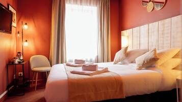 A hotel room with a large bed, a bedside table with a lamp, a chair, and a TV on the wall.