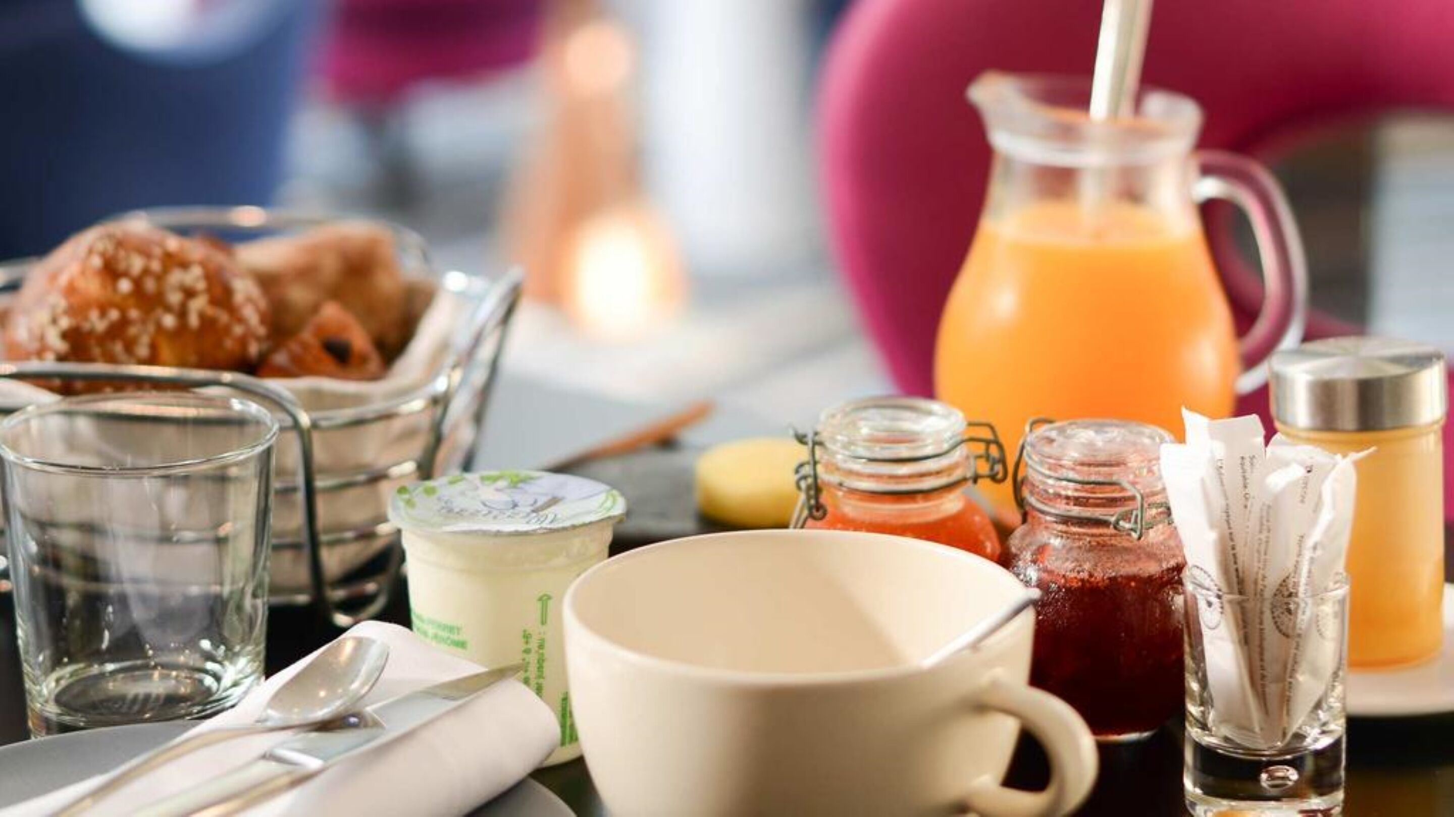 Una mesa de desayuno con diversos alimentos y bebidas, incluyendo una jarra de jugo de naranja, un vaso de leche y un tazón de cereal.